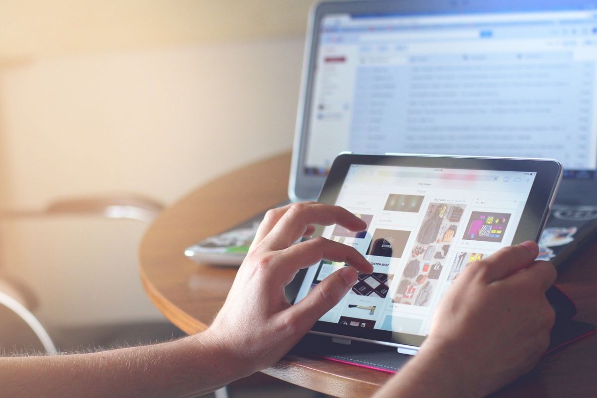 A hand scrolls down the screen of a tablet, with a computer in the background. Laser internet delivery could bring this level of access to everyone.