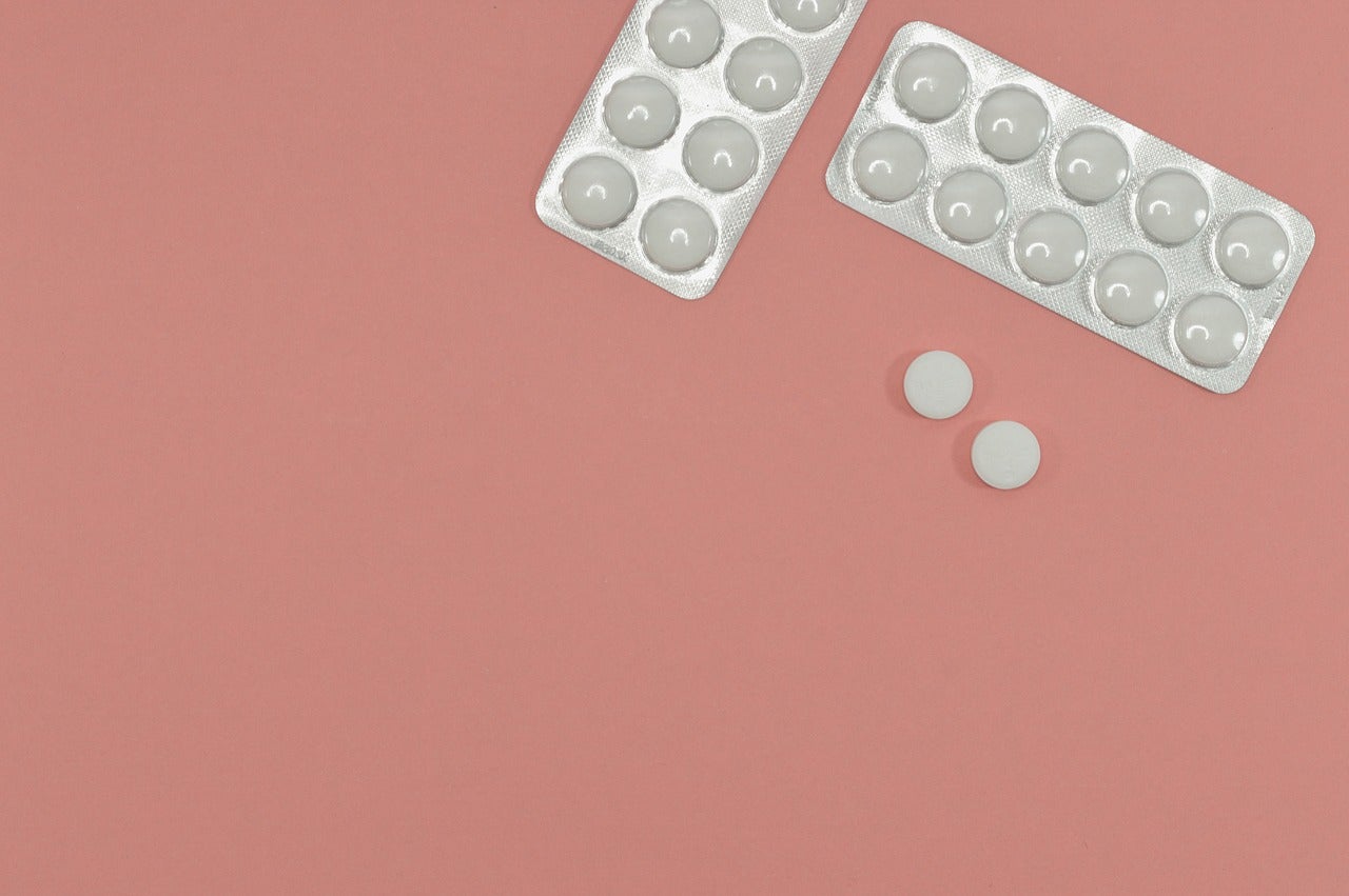 Two packs of white circular pills, and two loose pills, on a rose-pink background. A new antibiotic algorithm will hopefully reduce resistance to traditional drugs like these.