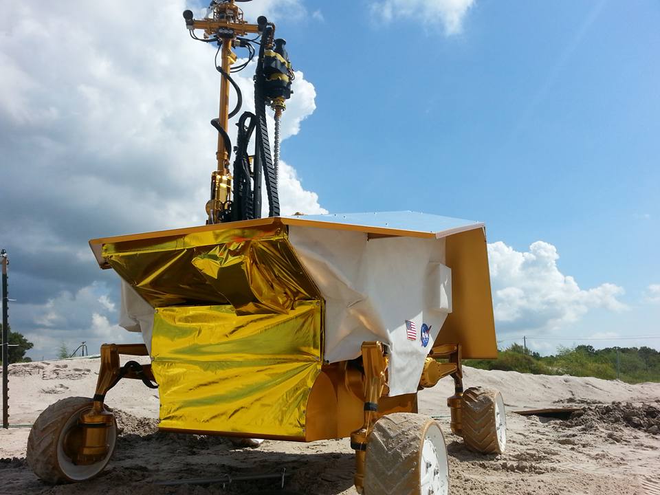 The Resource Prospector moon rover prototype, a four-wheeled square vehicle with gold foil at the front and a tall column of instruments at the top.